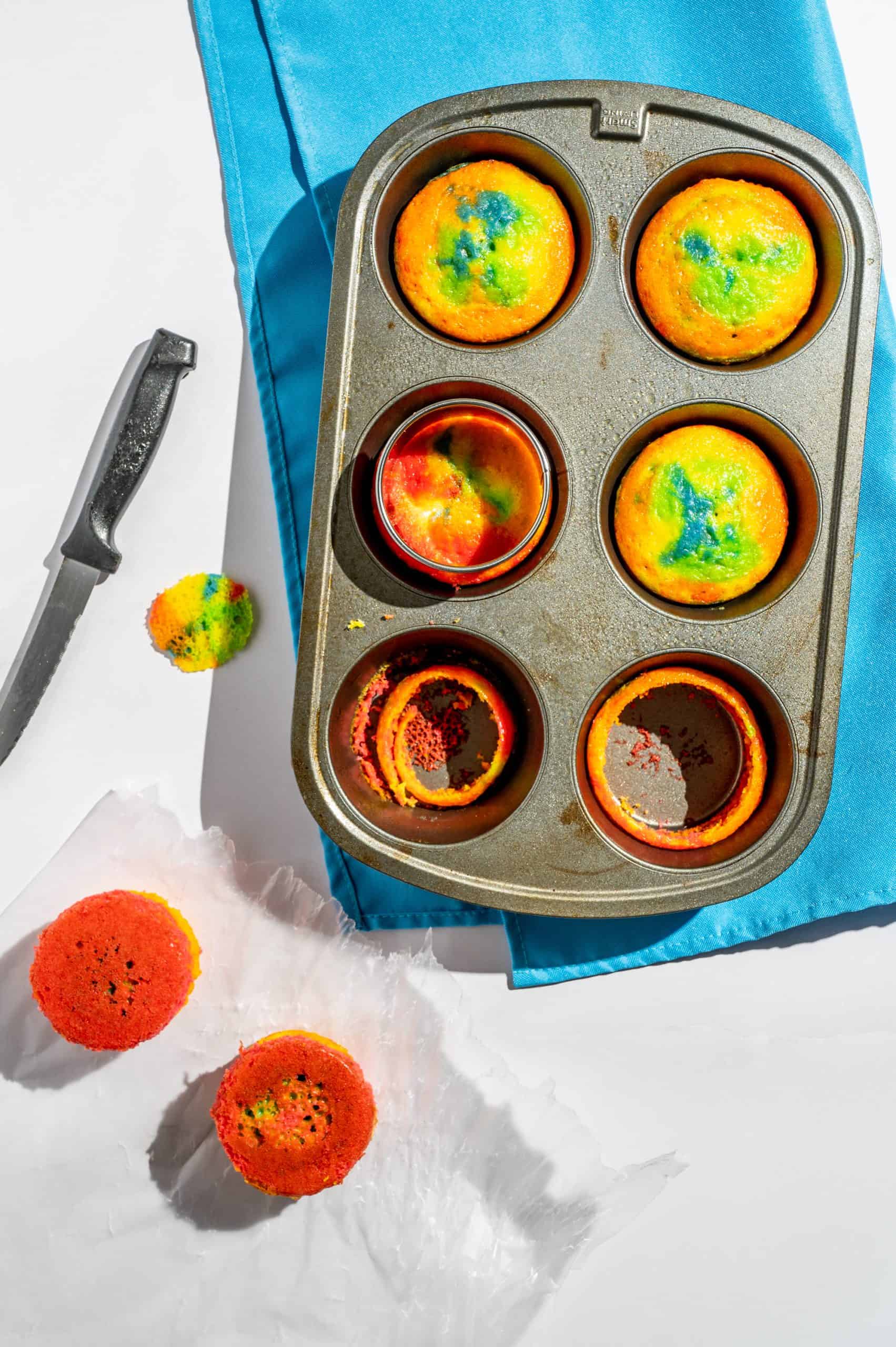 jumbo muffin tin with 6 large rainbow cupcakes being cut with a 3-inch cutter to make the sides straight