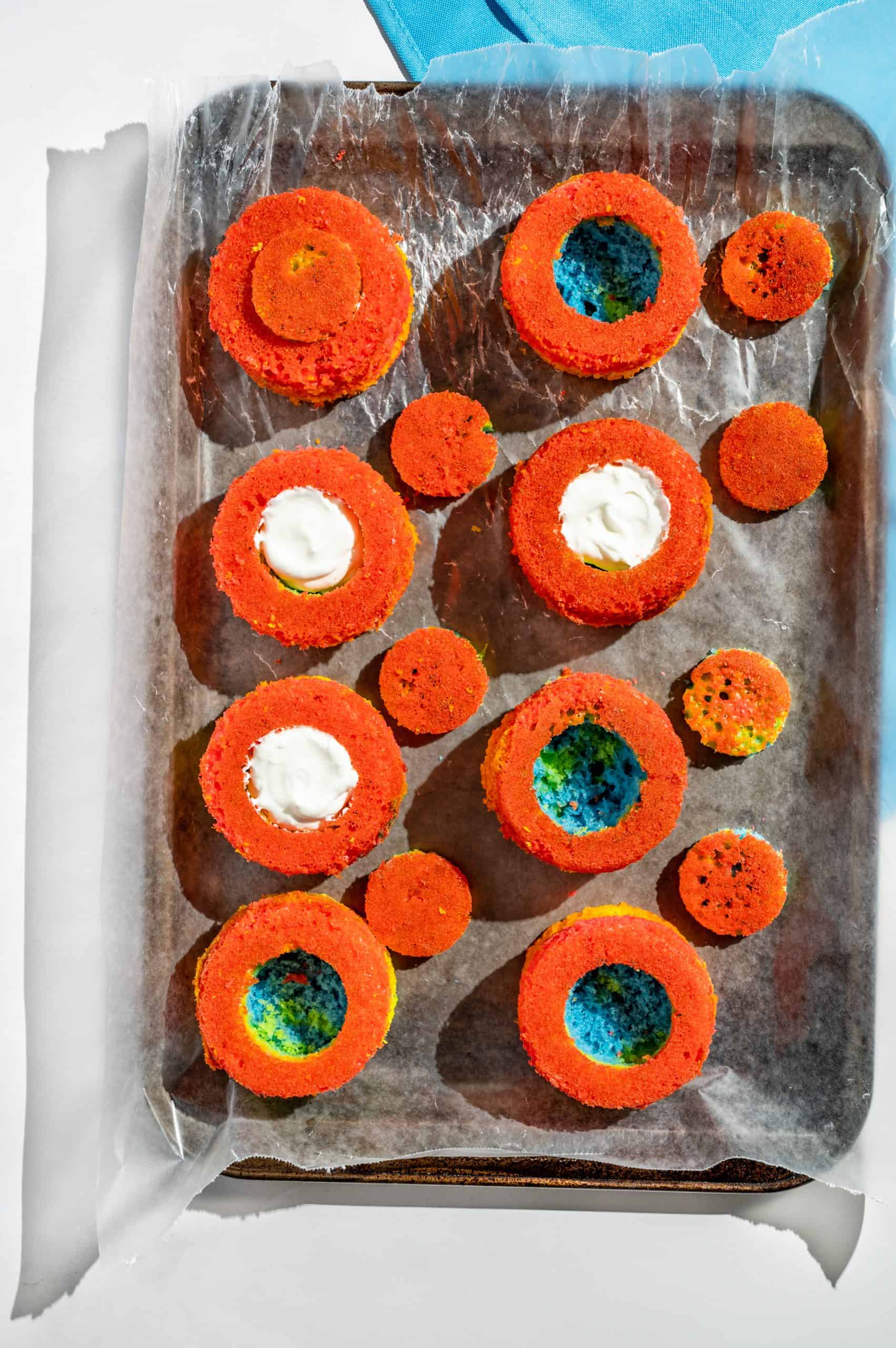 rainbow cupcakes with small circles cut out of each being filled with stabilized whipped cream