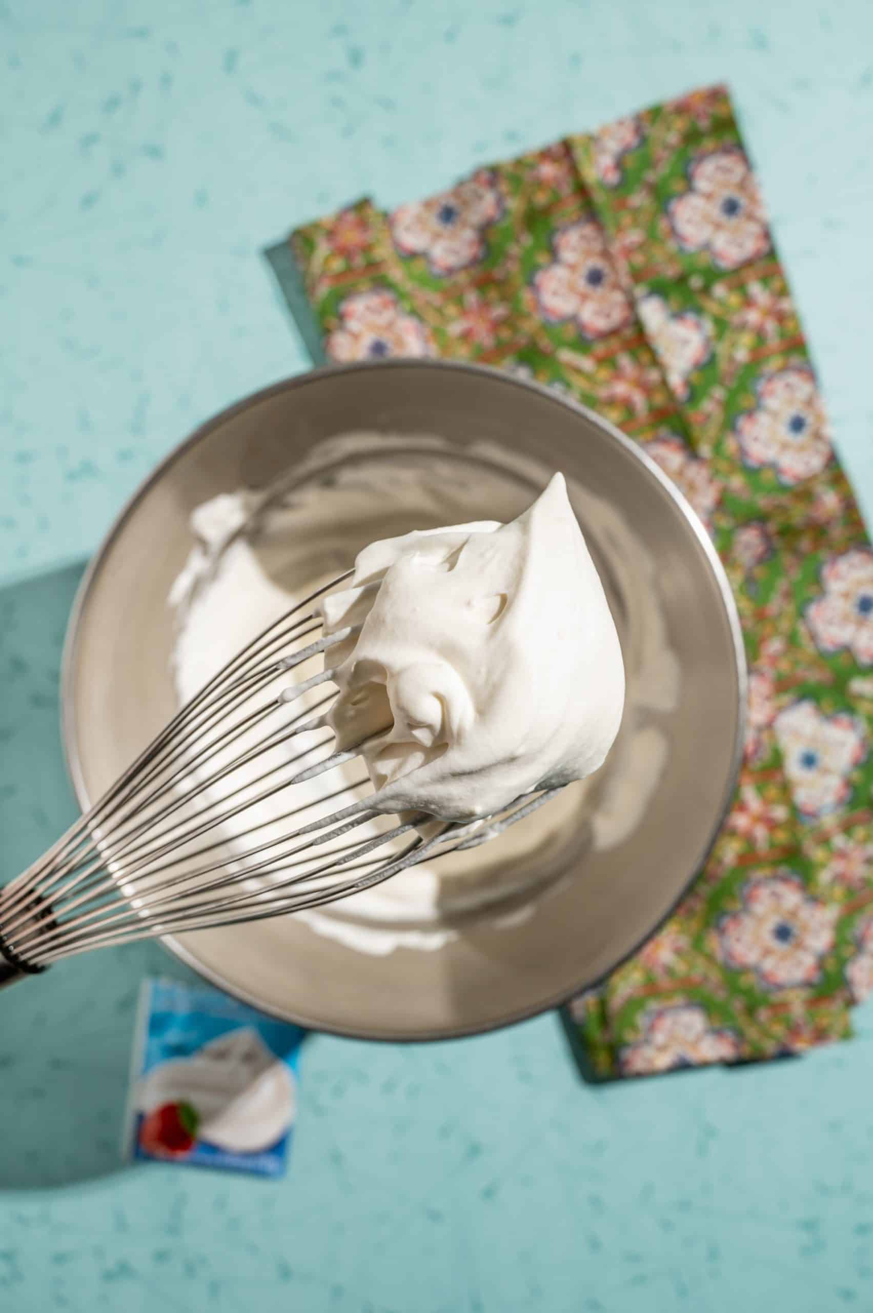 holding whisk above bowl showing freshly whipped cream with stabilizing agent