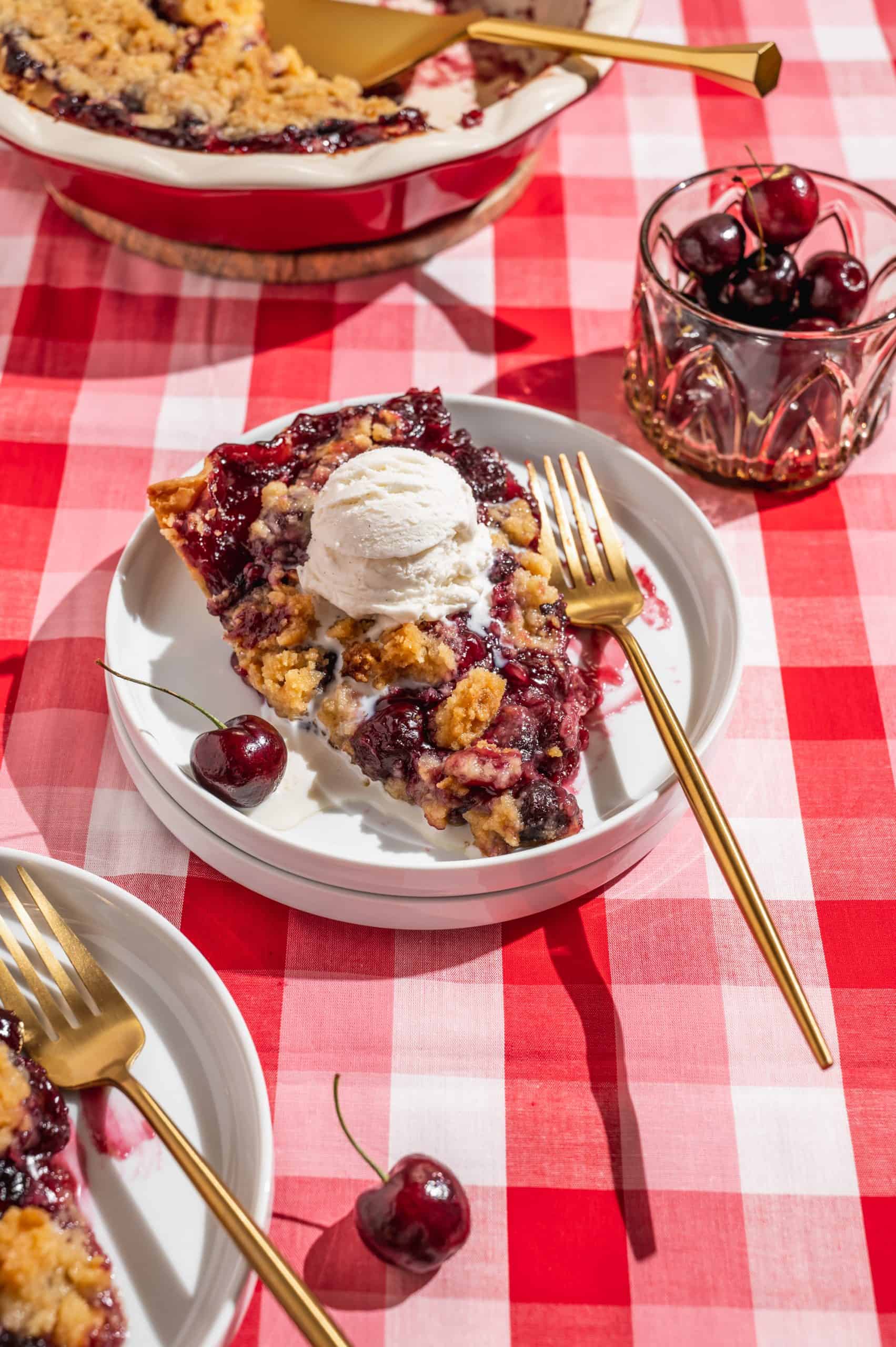 slice of cherry crumble pie with a scoop of vanilla ice cream melting on top