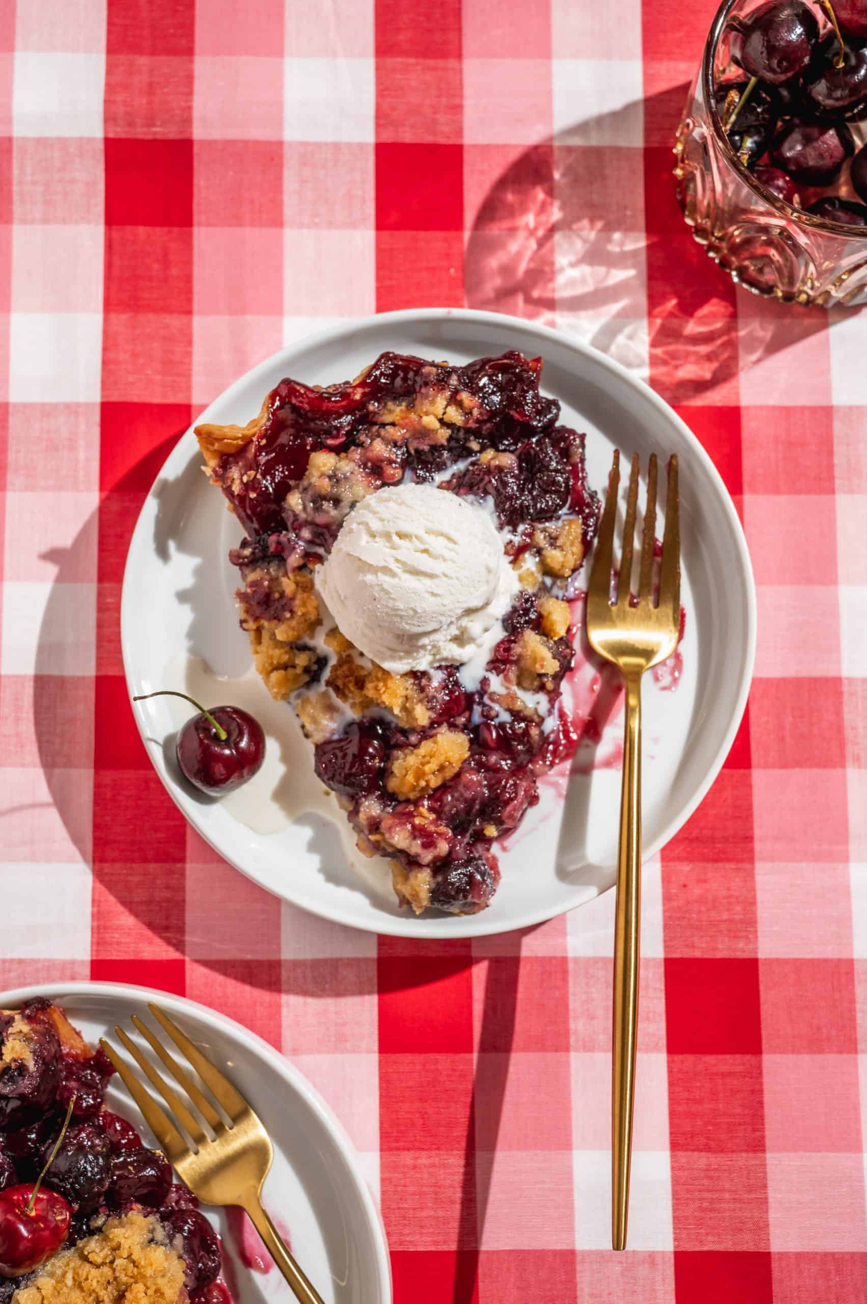 warm slice of cherry crumble pie with a scoop of vanilla ice cream melting on top