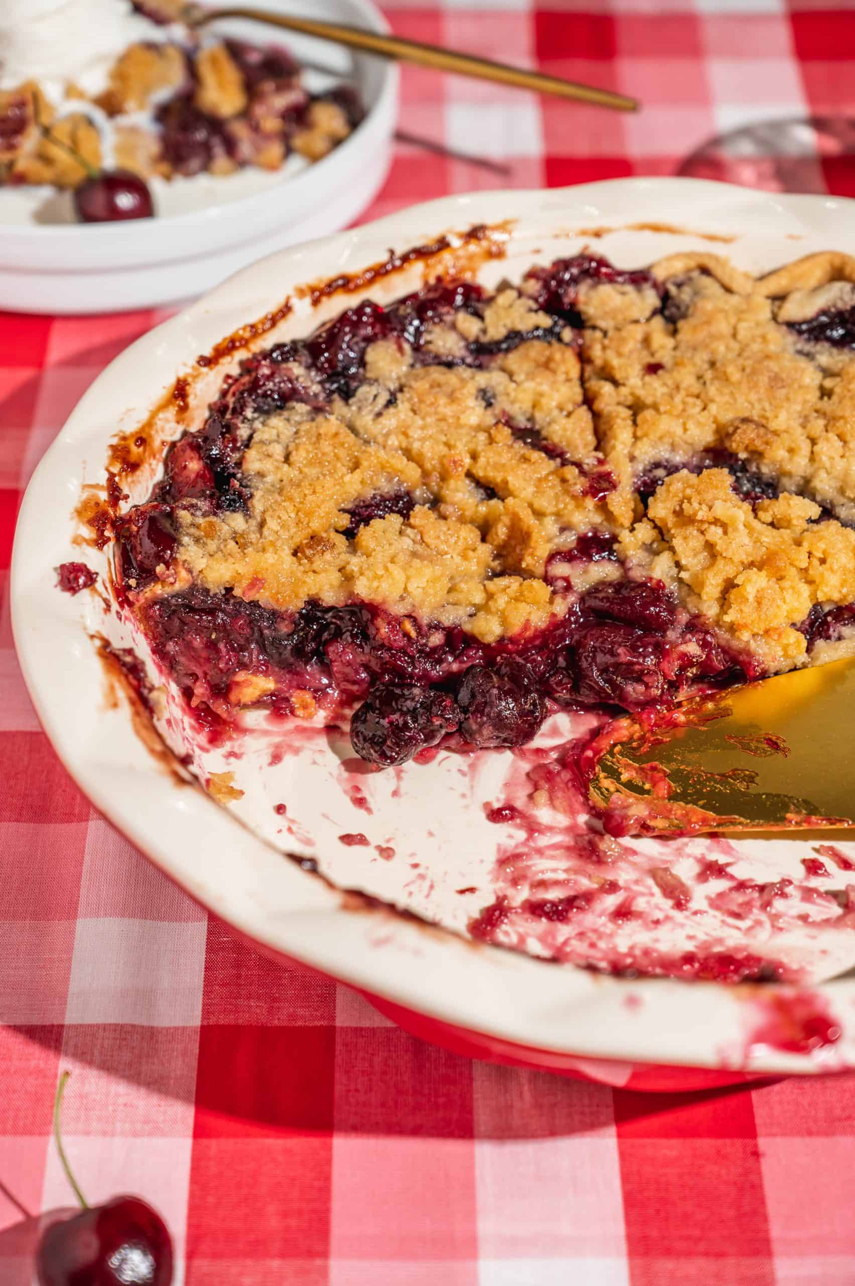 cherry crumble pie in red pie plate with a slice out to see filling