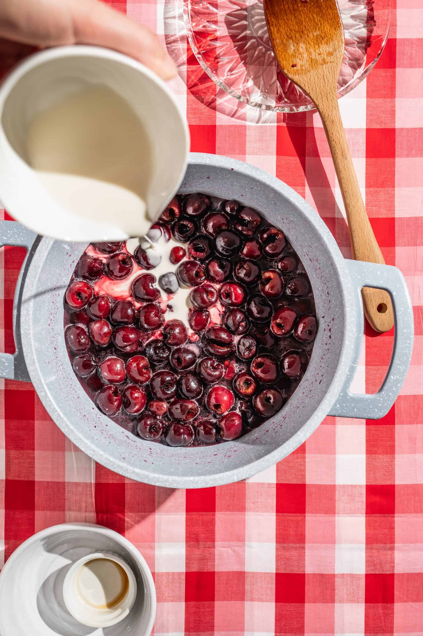 pouring cornstarch slurry into a pot with cooked pitted cherries