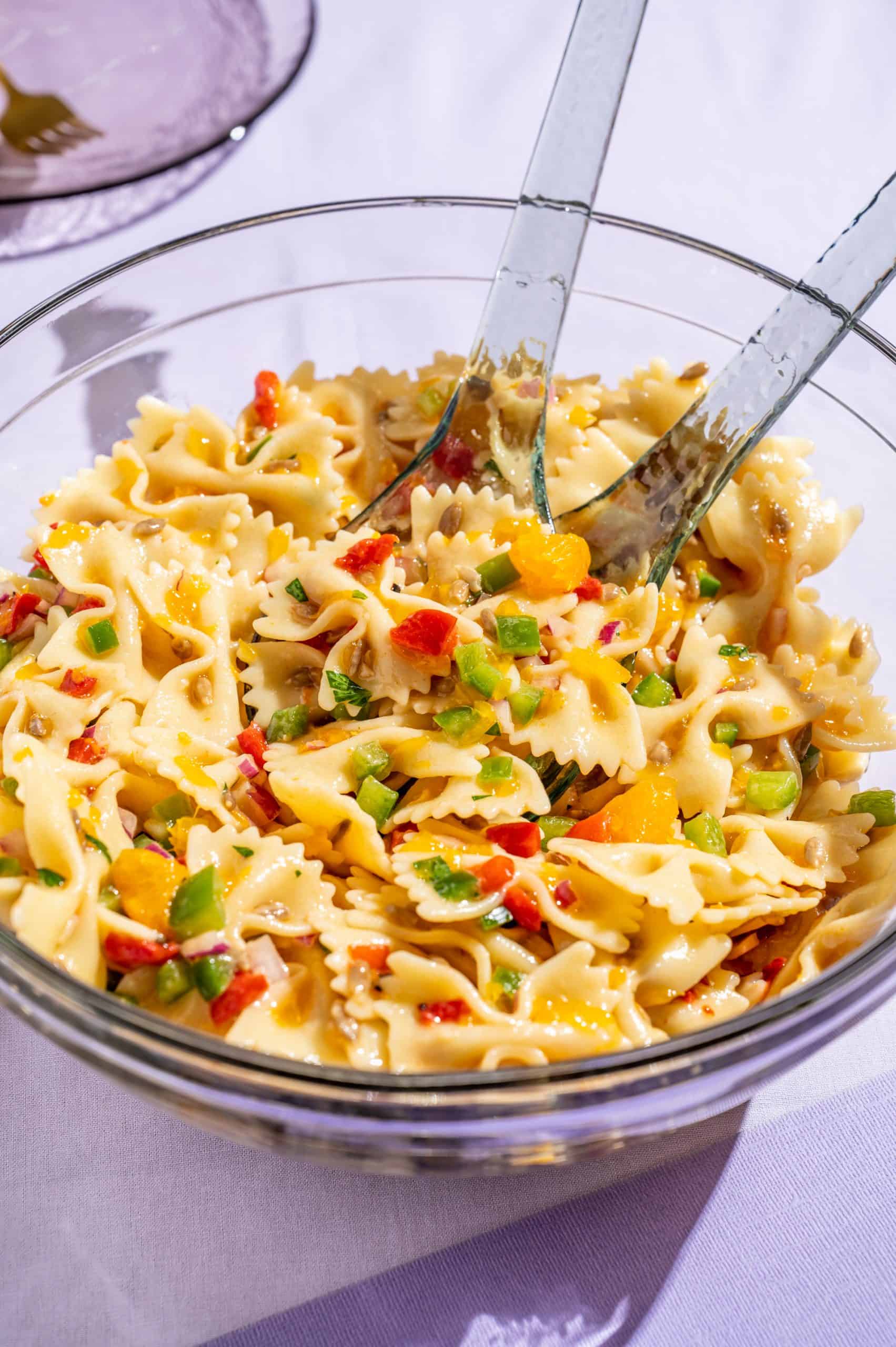 Honey pasta salad in a large glass bowl with serving tongs