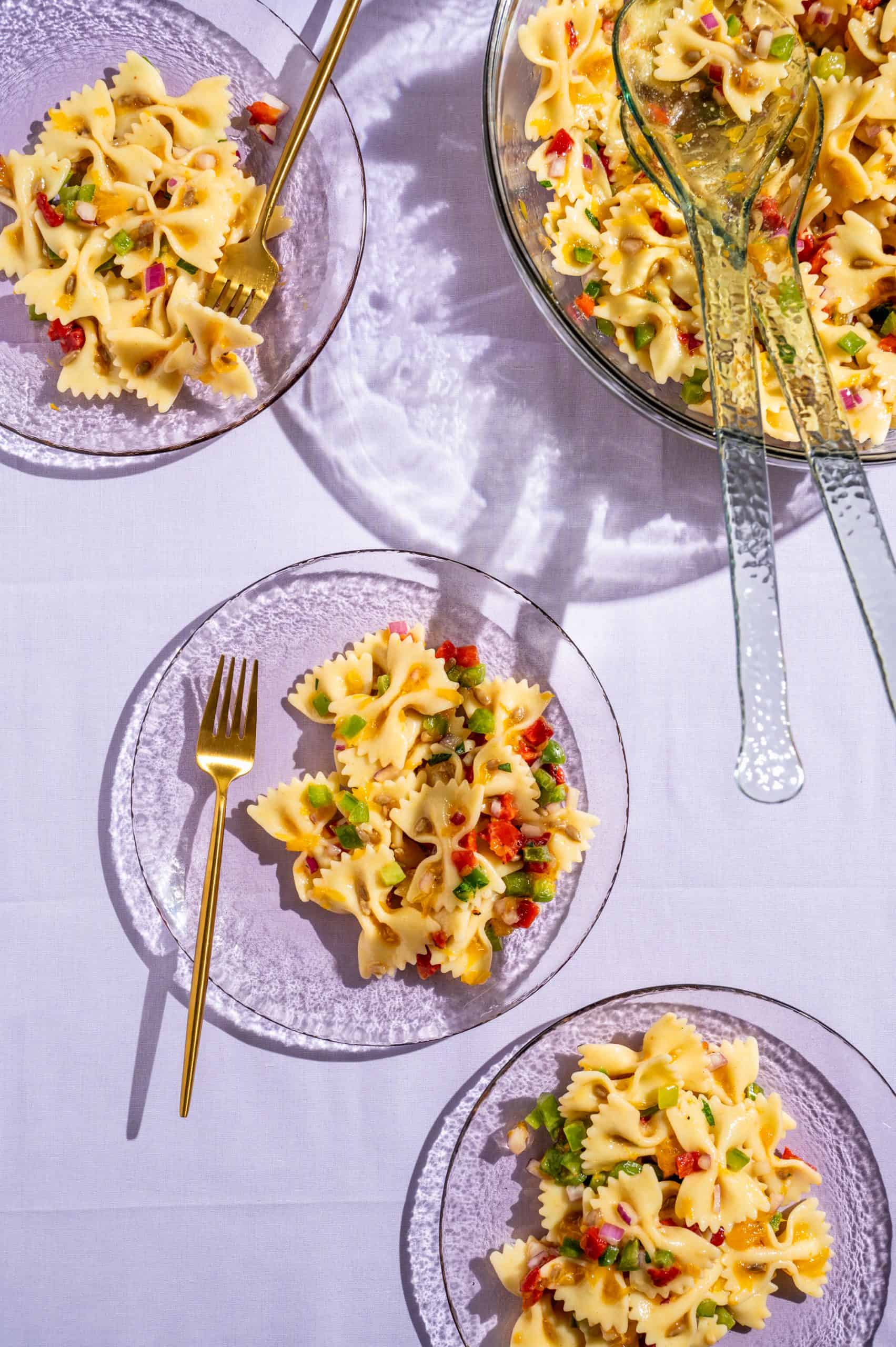 3 glass plates with honey pasta salad on light purple tablecloth