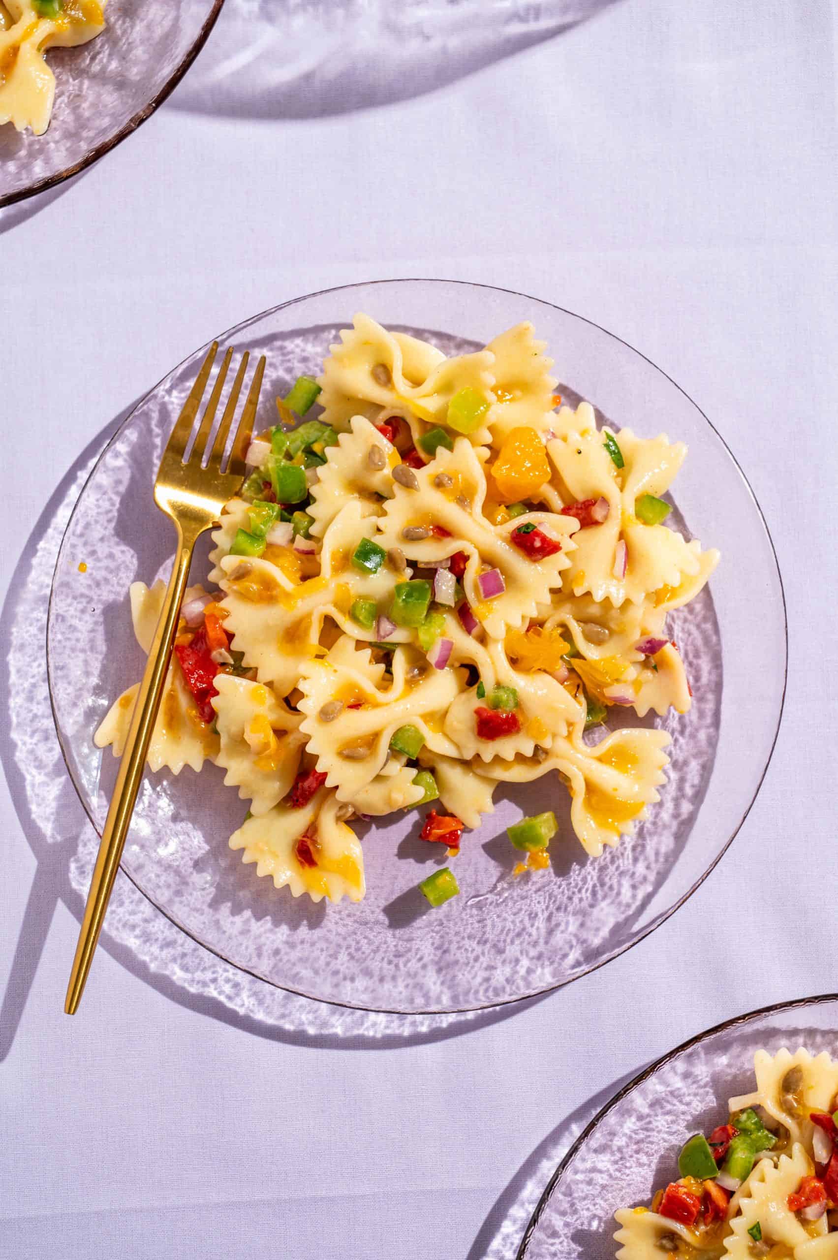 Honey pasta salad on a glass plate set on a light purple tablecloth