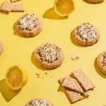 lemon meringue cookies on a yellow surface surrounded by lemon halves and graham cracker pieces