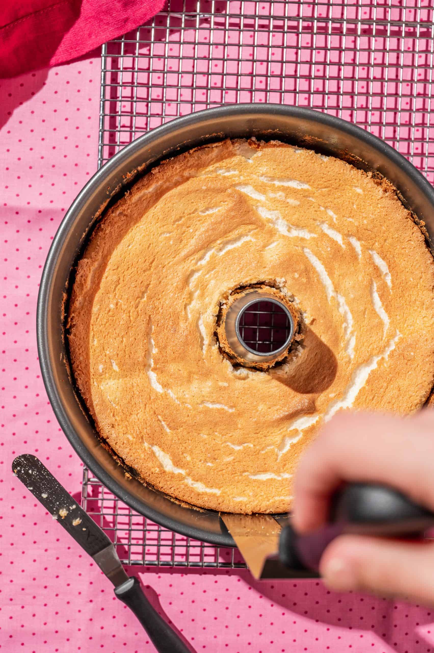 cutting around outside of a baked angel cake in a tube pan with an icing spatula