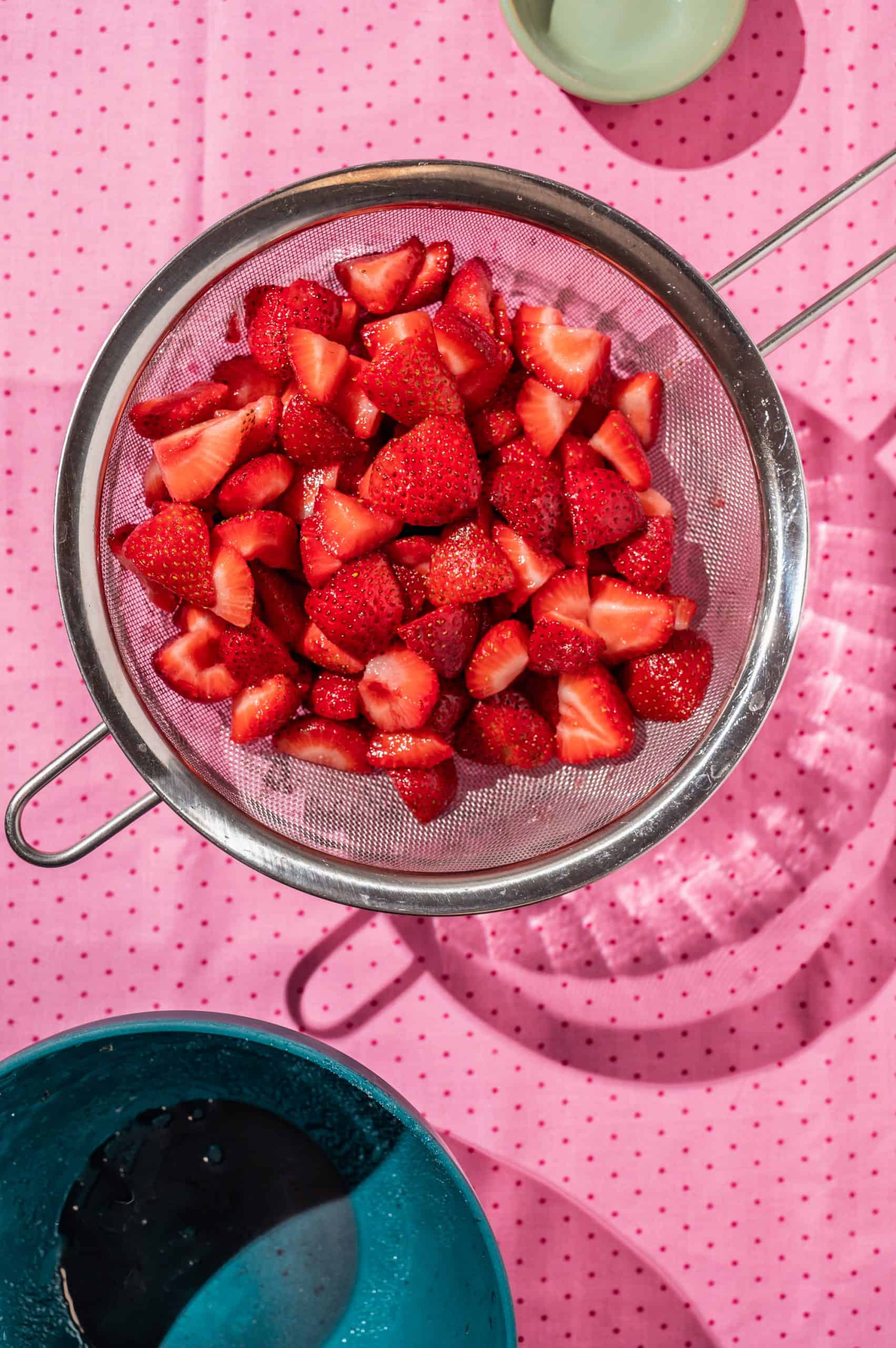 macerated strawberries in a strainer over a bowl to catch juices