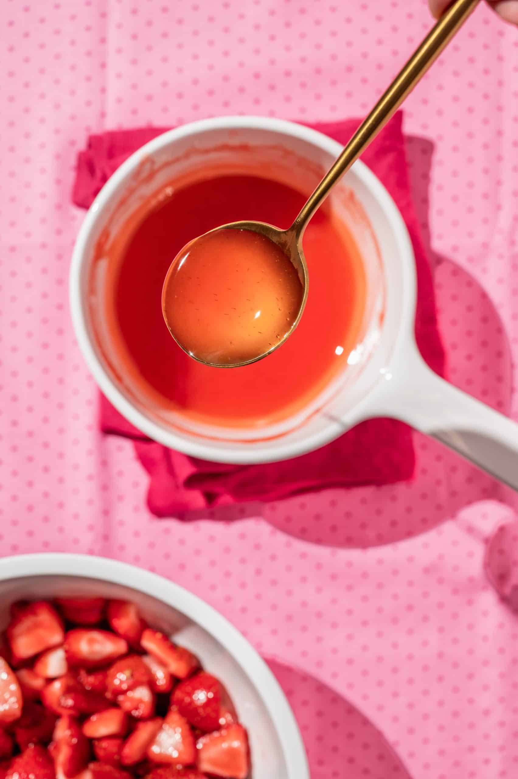 holding a spoon above pot of strawberry juice thickened with cornstarch to make a syrup