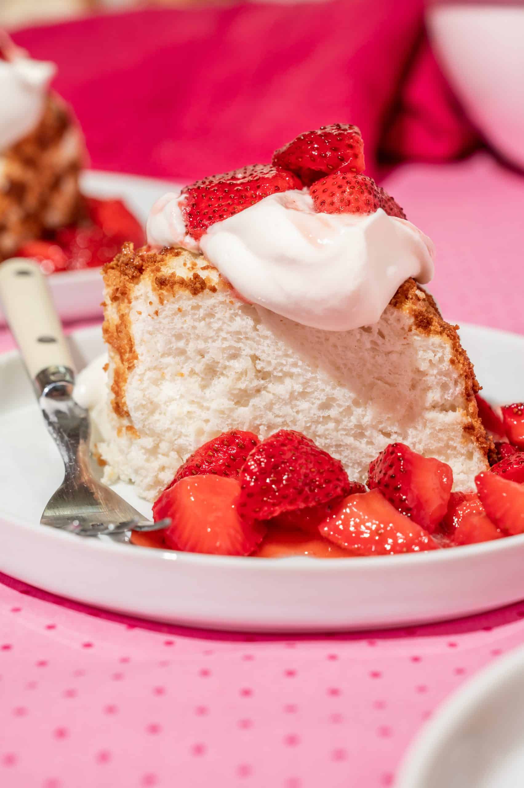 a slice of angel cake on a plate with fresh whipped cream and strawberry topping