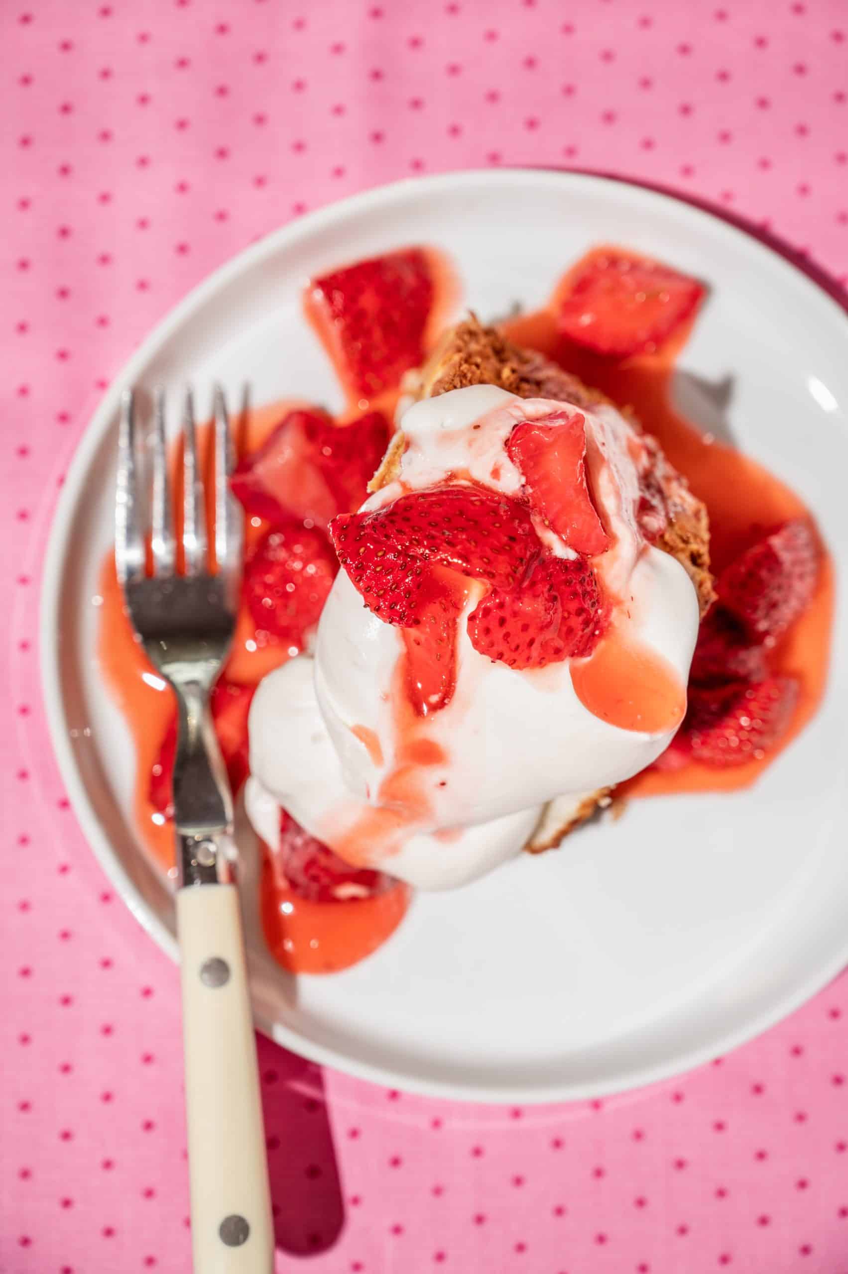 a slice of angel cake topped with whipped cream and strawberries in syrup