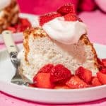 a slice of angel cake on a plate with fresh whipped cream and strawberry topping