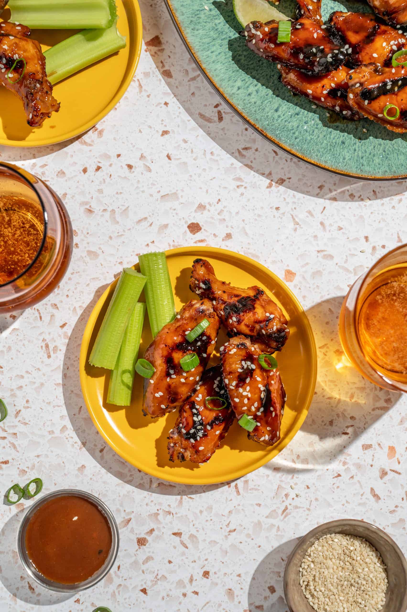 Small plate with 4 Asian grilled chicken wings and celery, glasses of beer, and platter with extra wings on the side