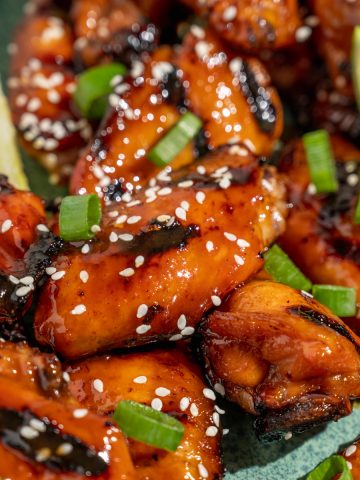 Close up of Asian grilled chicken wings with sesame seeds, scallions, and lime wedges on a platter
