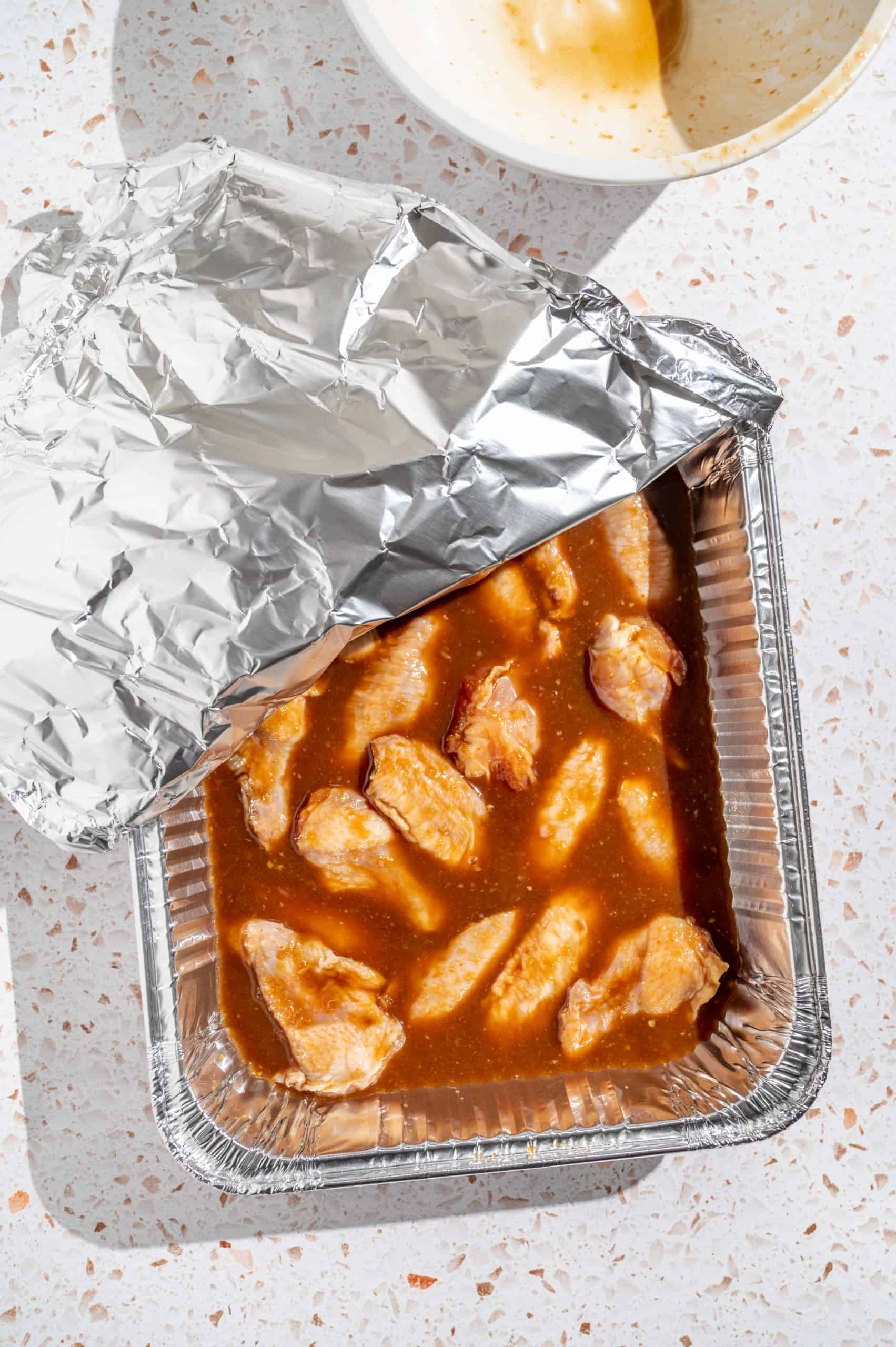 Raw chicken wings in Asian marinade in a grill pan, half covered with foil