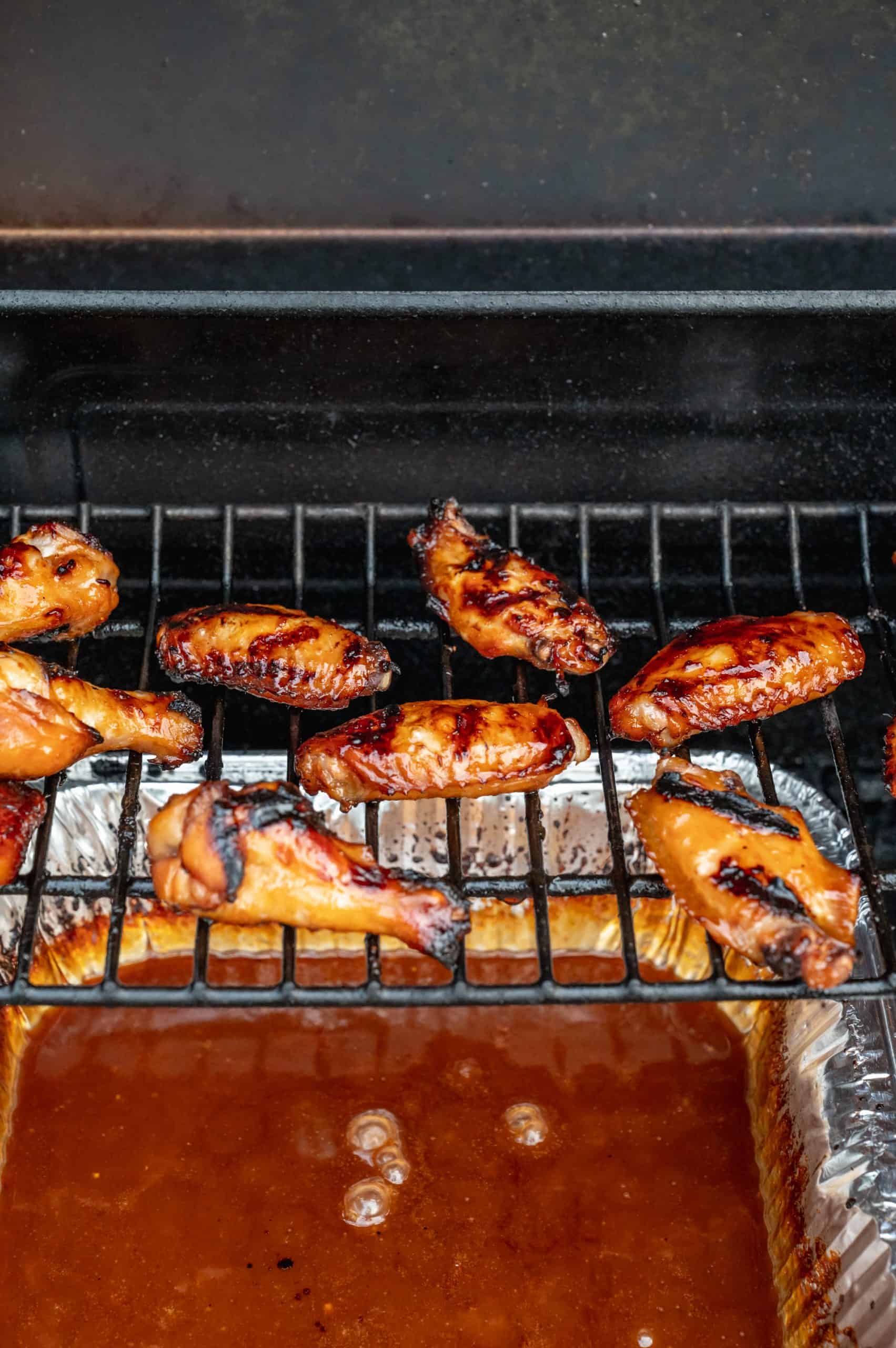 8 chicken wings on the upper grill rack over a grill pan with Asian sauce, bubbling