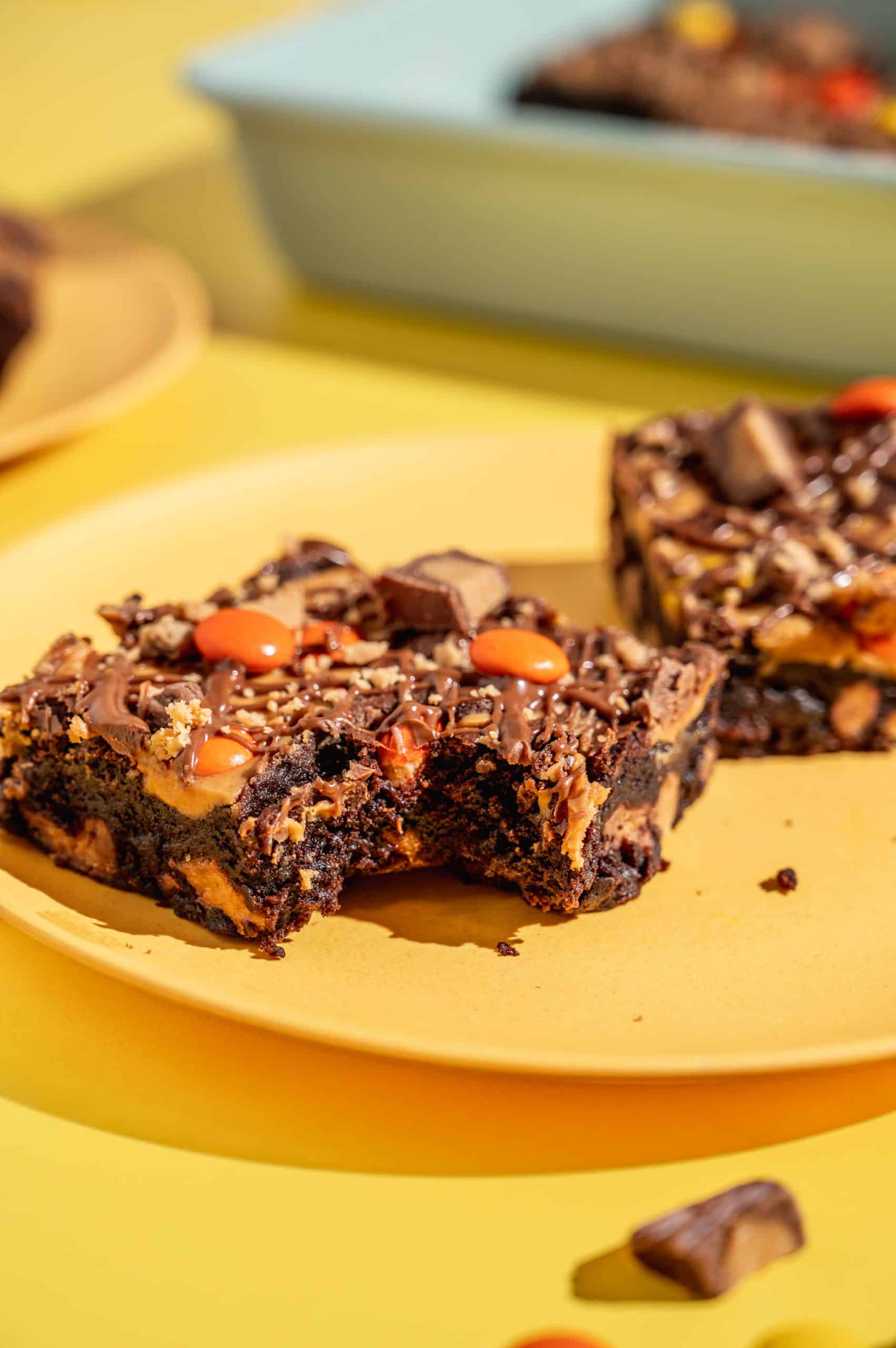 Close-up of a Reese's brownie with a bite taken out on a yellow plate showing fudgy interior.