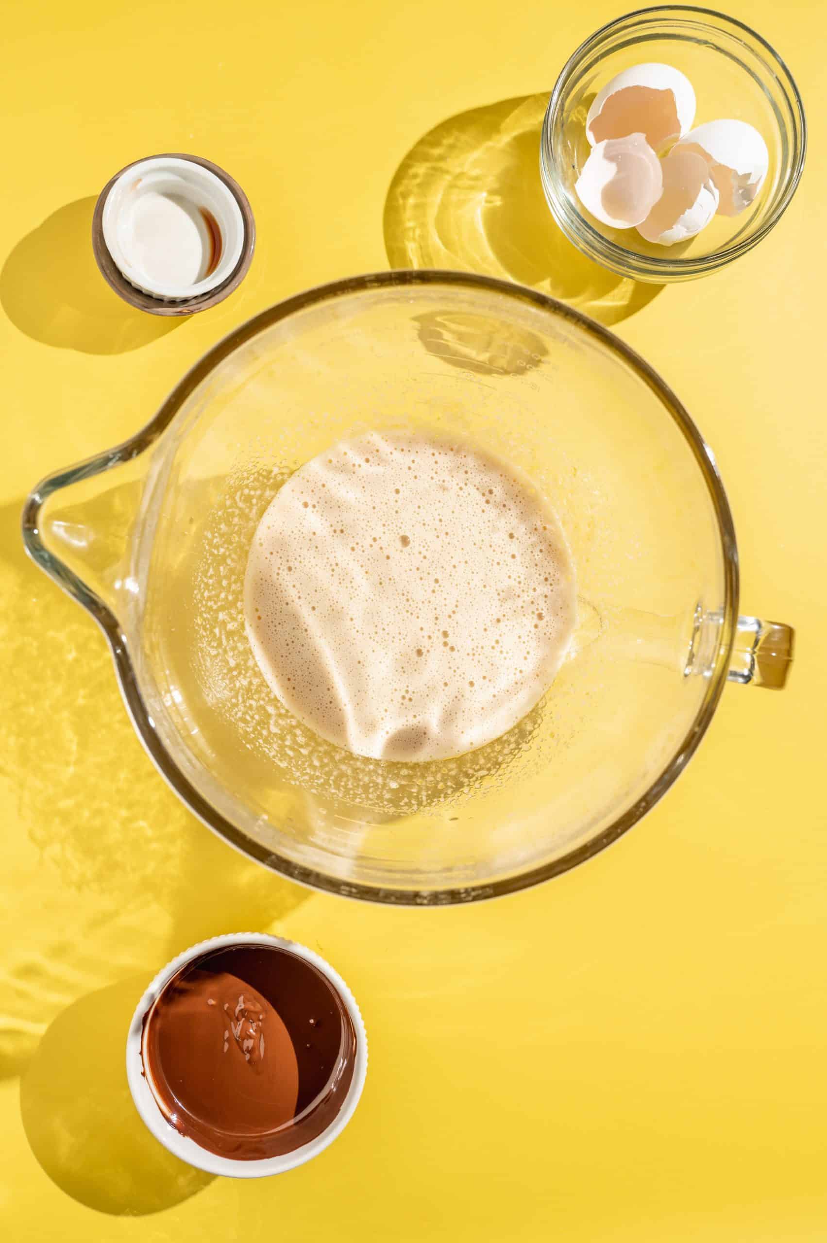 Glass mixing bowl with eggs, sugar, salt, water, and vanilla mixed together.