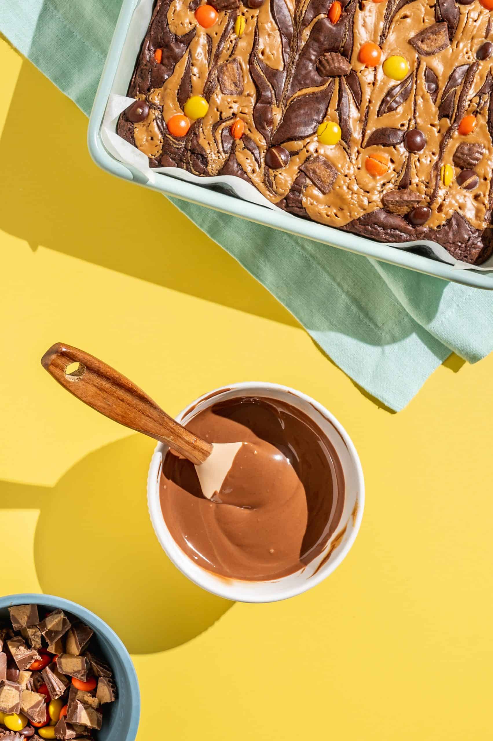 Peanut butter and melted chocolate mixed together in a small bowl, tray of Reeses brownies on the side.