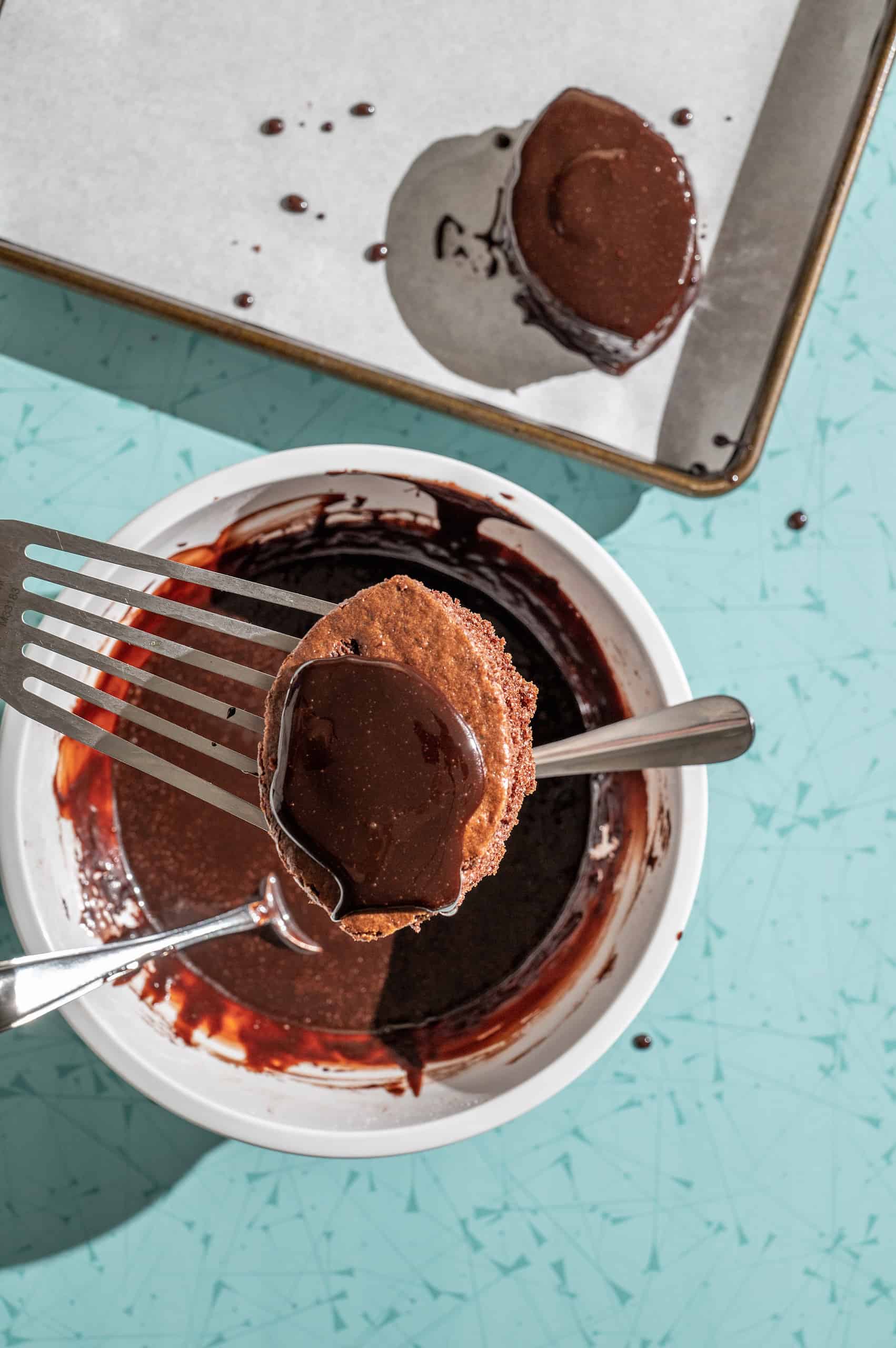 dipping mini chocolate football cake into chocolate glaze coating