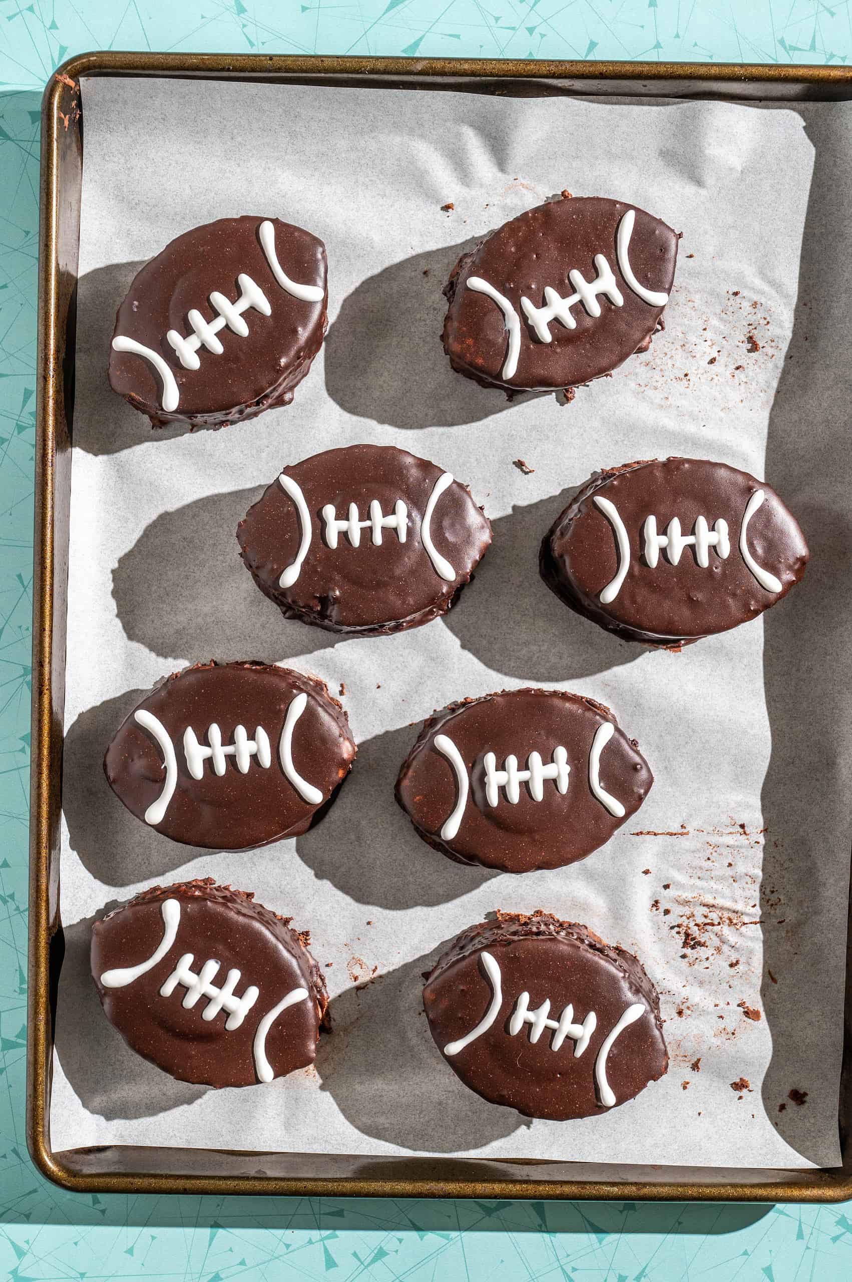 8 mini chocolate football cakes on a tray after decorating with white icing